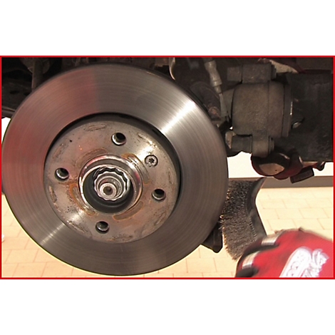 Nahaufnahme einer Bremsscheibe, teilweise mit Rost, im Fokus. Im Hintergrund der Bremssattel und ein Pinsel.